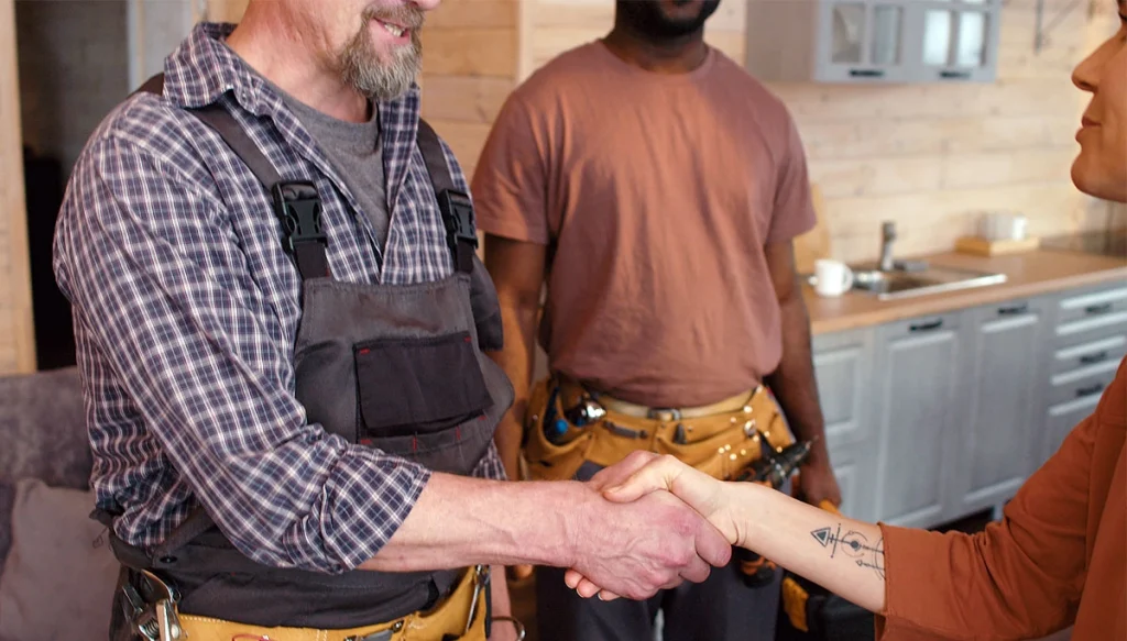 woman shaking hands with a plumber with his assistant is in the back